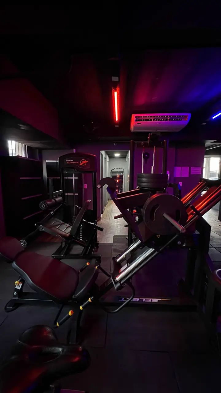 Salão de treino da AG Force com esteiras e aparelhos sob luzes de LED roxas, azuis e vermelhas
