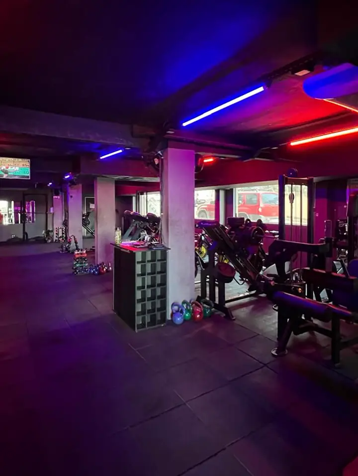Área de funcional com kettlebells, anilhas e aparelhos, iluminada por LED azul e vermelho