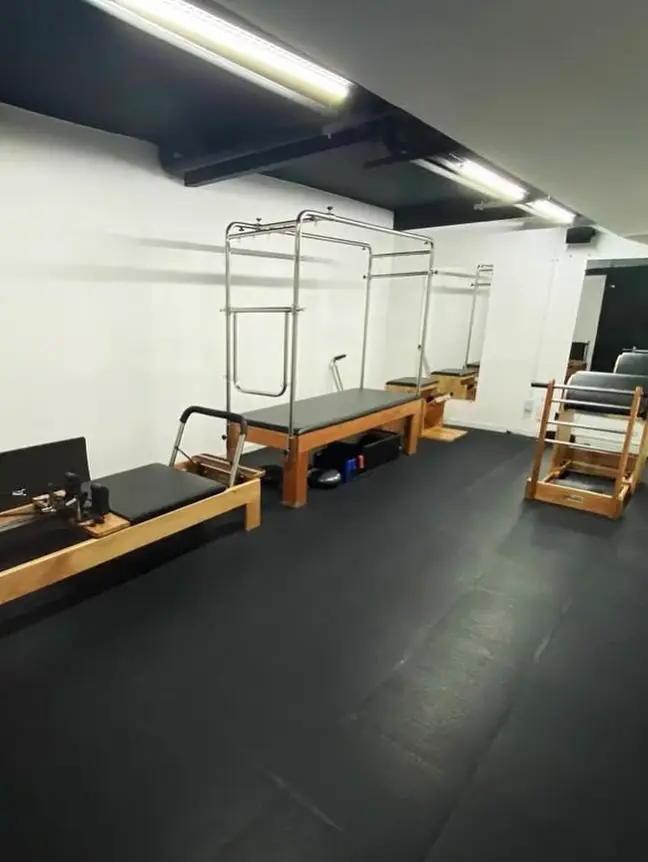 Estúdio de pilates em sala clara, com aparelhos de pilates de madeira e estrutura metálica